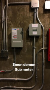 Two gray electrical boxes with metal conduit pipes mounted on a brown wall, labeled Eaton and Honeywell, with the text 
