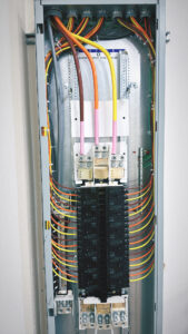 An open electrical panel showing circuit breakers and neatly organized colored wiring inside a metal enclosure.