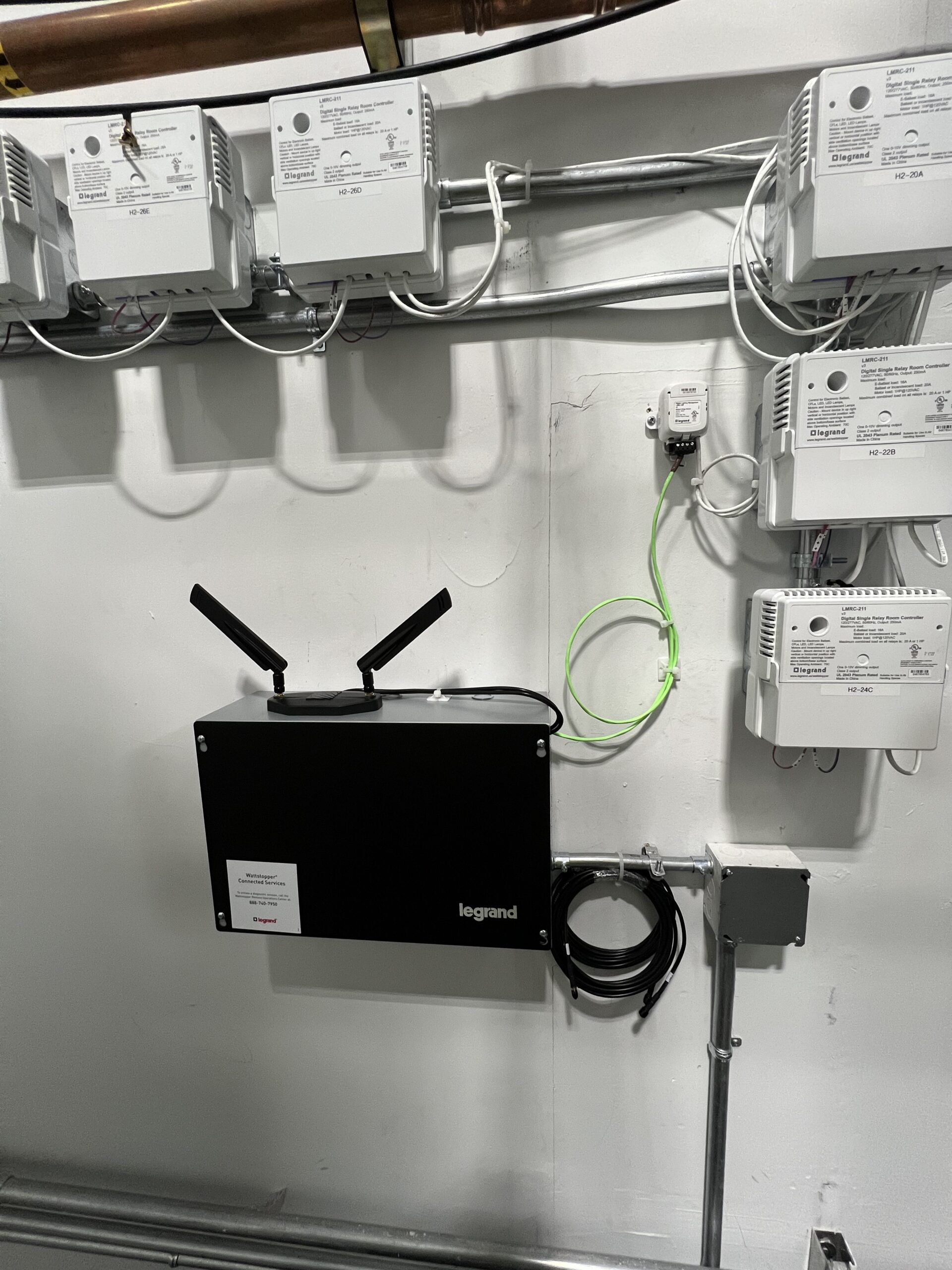 A black Legrand device with two antennas is mounted on a wall below six white electrical units; cables and wires are organized around the setup.