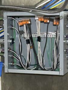 Open electrical junction box showing multiple black, white, and green wires connected with push-in wire connectors and secured to grounding bars.