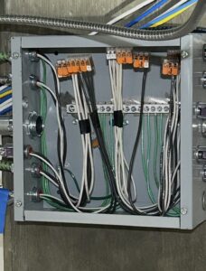 An open electrical junction box with multiple wires of various colors connected to terminals and connectors inside.