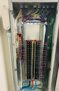 An open electrical panel shows multiple circuit breakers, neatly arranged wires, and a notice to install with the indicated end up.