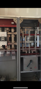 An electrical panel with exposed metal busbars, switches, circuit breakers, and a large ON/OFF switch at the bottom right.