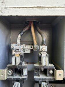 Close-up of an electrical panel showing damaged, burned, and frayed wiring connected to terminals.