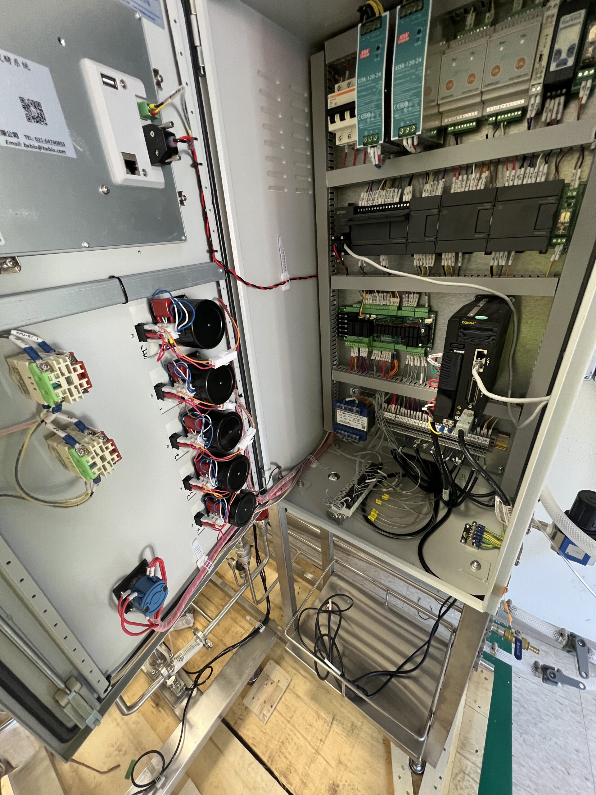 Open electrical control panel showing various circuits, wiring, relays, fuses, circuit boards, and electronic components mounted inside a metal enclosure.